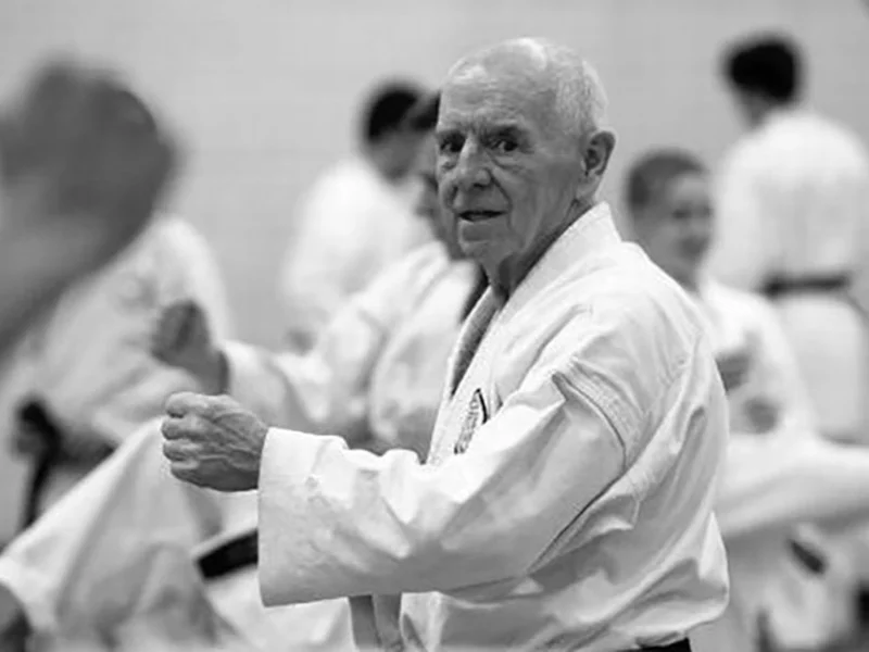 Practicante de karate mayor practicando en un dojo, rodeado de otros karatekas durante un entrenamiento, con un gesto concentrado