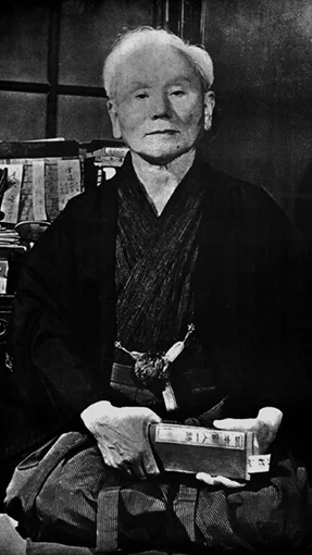 Foto de Gichin Funakoshi, fundador del Karate moderno, con libros en sus manos, representando la filosofía y enseñanza del Karate-Do